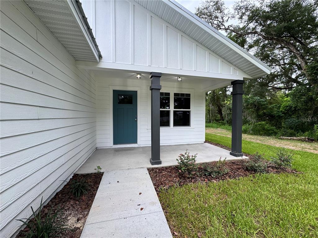 A white house exterior features a covered porch with dark columns and a teal door — 8507 SE 70TH AVENUE, TRENTON, FL