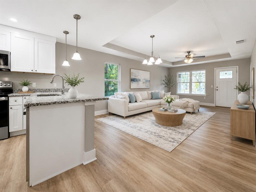 An open-concept kitchen and living room featuring white cabinetry, granite countertops, and light wood flooring — 8507 SE 70TH AVENUE, TRENTON, FL