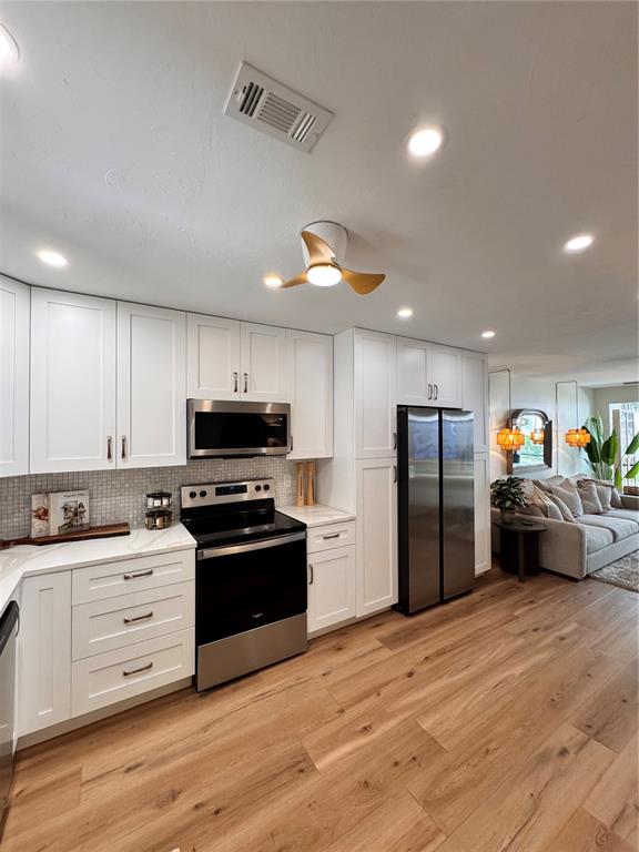 A modern kitchen features white cabinetry, stainless steel appliances, and light wood flooring — 5623 MIDNIGHT PASS ROAD UNIT 615, SIESTA KEY, FL