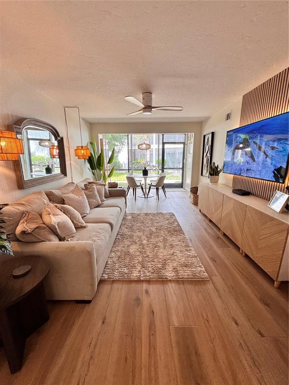 A living room features a beige sofa, wood flooring, a wall-mounted television, and dining area — 5623 MIDNIGHT PASS ROAD UNIT 615, SIESTA KEY, FL