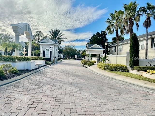 A paved driveway leads toward the entrance gate of a residential community with palm trees — 330 SOUTHERN PECAN CIRCLE UNIT 208, WINTER GARDEN, FL