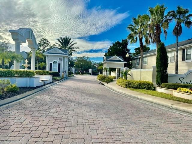 A paved driveway leads toward the gated entrance of a residential community with palm trees — 330 SOUTHERN PECAN CIRCLE UNIT 208, WINTER GARDEN, FL