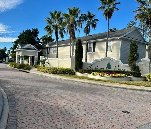 The exterior of a residential community entrance features a sign, palm trees, and landscaping — 330 SOUTHERN PECAN CIRCLE UNIT 208, WINTER GARDEN, FL