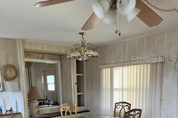 A dining area features wood-paneled walls, a ceiling fan, a chandelier, and vertical window blinds — 3203 BIRKDALE DRIVE, HOLIDAY, FL