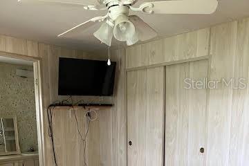 A bedroom features wood-paneled walls, a ceiling fan, a wall-mounted television, and sliding closet doors — 3203 BIRKDALE DRIVE, HOLIDAY, FL