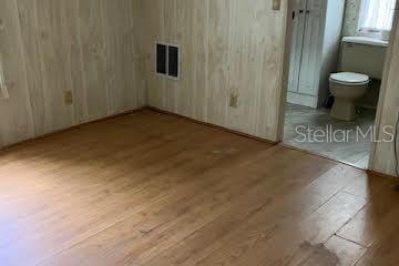 A room with wood-paneled walls and wood-look flooring leads into a bathroom with a toilet — 3203 BIRKDALE DRIVE, HOLIDAY, FL