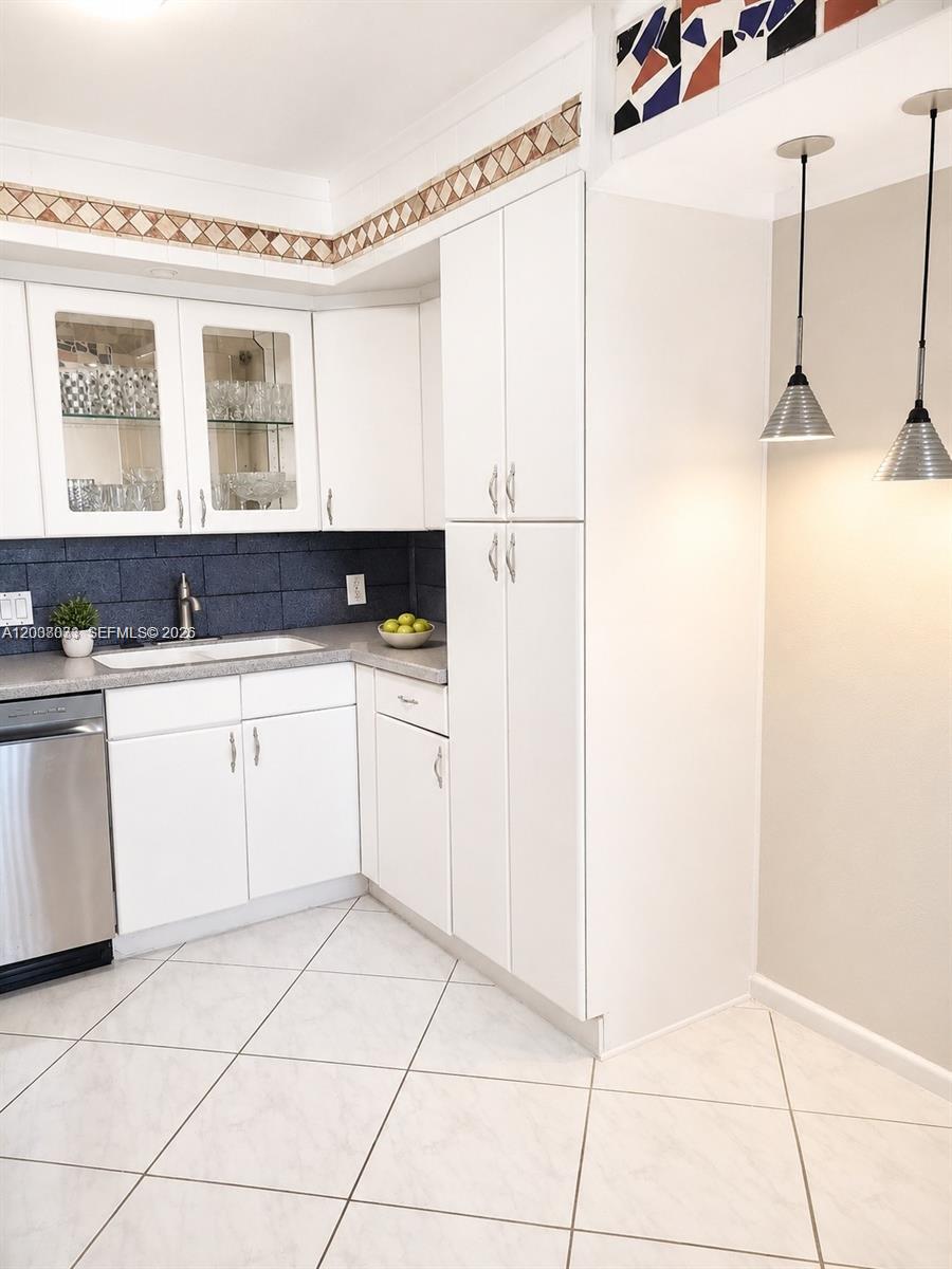 A kitchen features white cabinets, a dark blue backsplash, and two hanging pendant lights — 2050 Newcastle C # 2050, Boca Raton FL 33434, BOCA RATON, FL