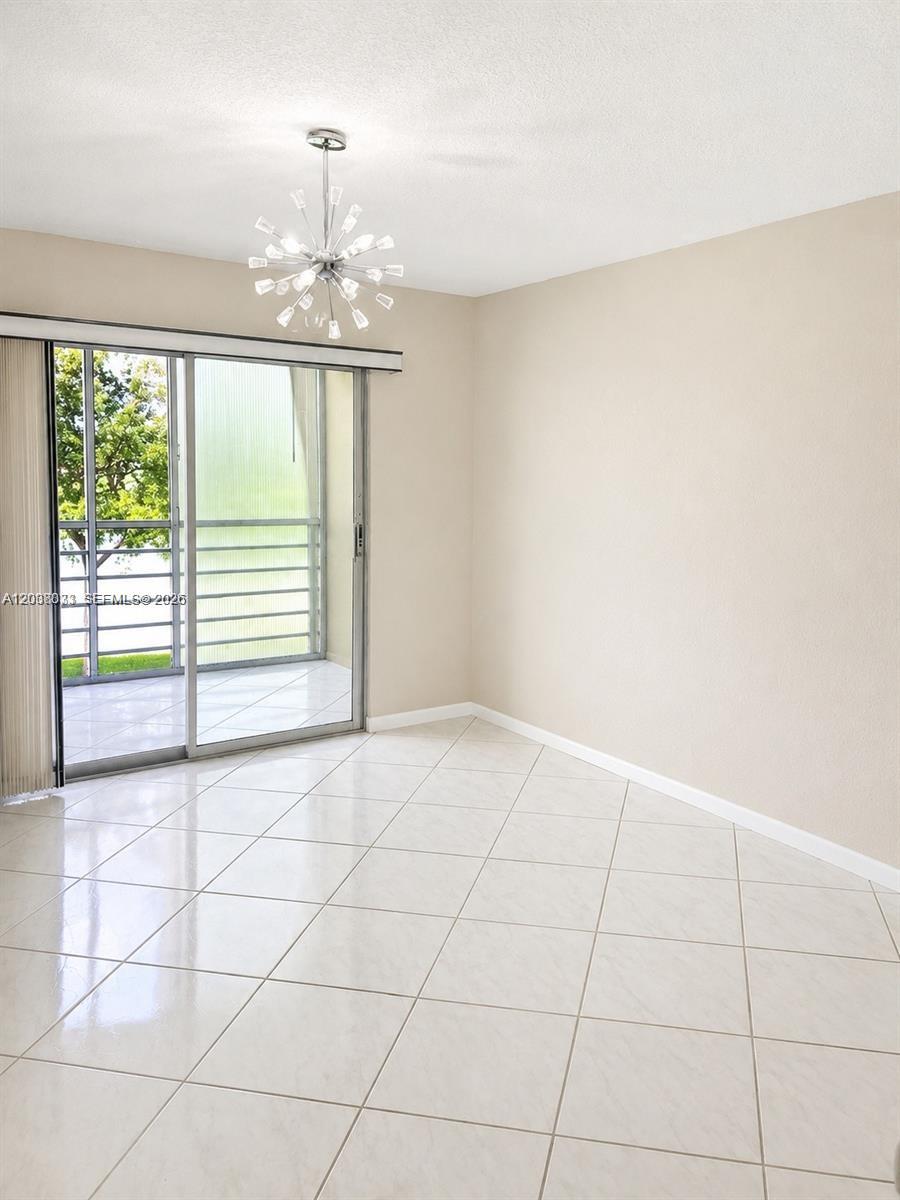 A dining area features light-colored tile flooring, a modern chandelier, and a sliding glass door — 2050 Newcastle C # 2050, Boca Raton FL 33434, BOCA RATON, FL
