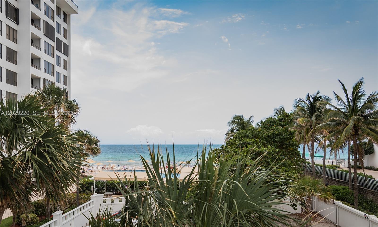 A view of the ocean and pool area from a balcony with palm trees — 3505 S Ocean Dr # 221, Hollywood FL 33019, HOLLYWOOD, FL