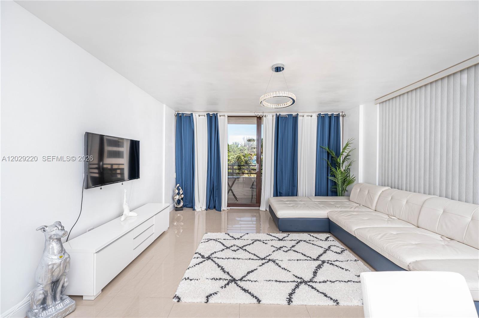 A living room features a white sectional sofa, a television, and blue and white curtains — 3505 S Ocean Dr # 221, Hollywood FL 33019, HOLLYWOOD, FL