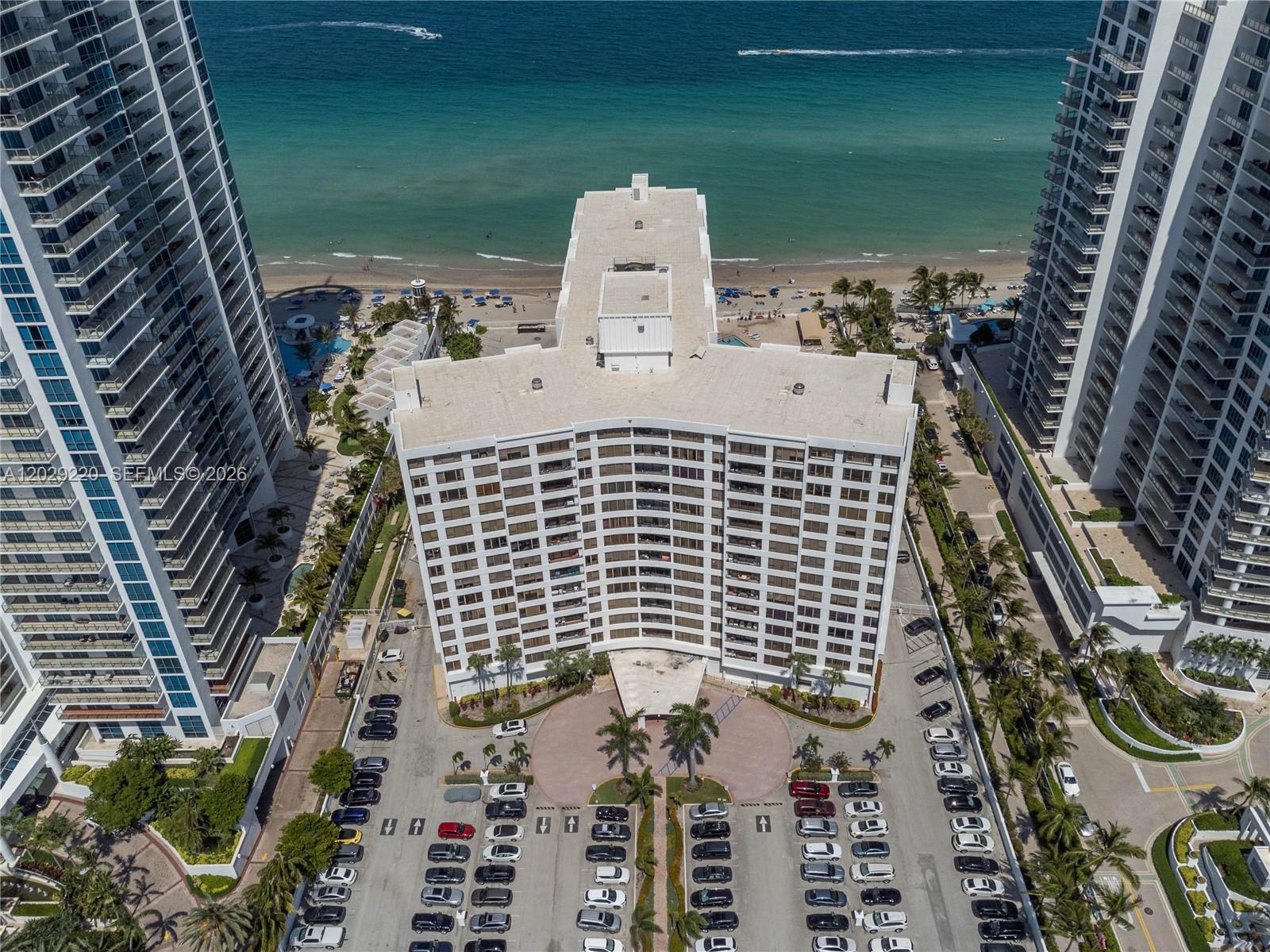 An aerial view shows a high-rise residential building surrounded by a parking lot and beach — 3505 S Ocean Dr # 221, Hollywood FL 33019, HOLLYWOOD, FL