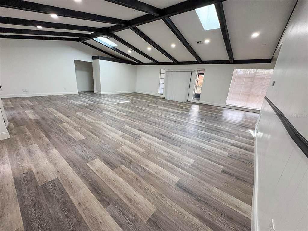A large, empty room features vaulted ceilings with dark exposed beams and wood-look flooring — 3810 SE 22ND PLACE, OCALA, FL