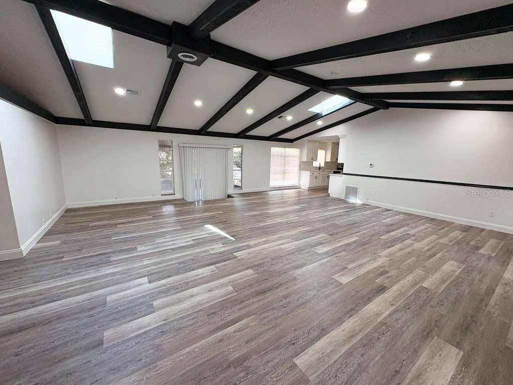 A spacious living room features vaulted ceilings with dark exposed beams and wood-look flooring — 3810 SE 22ND PLACE, OCALA, FL