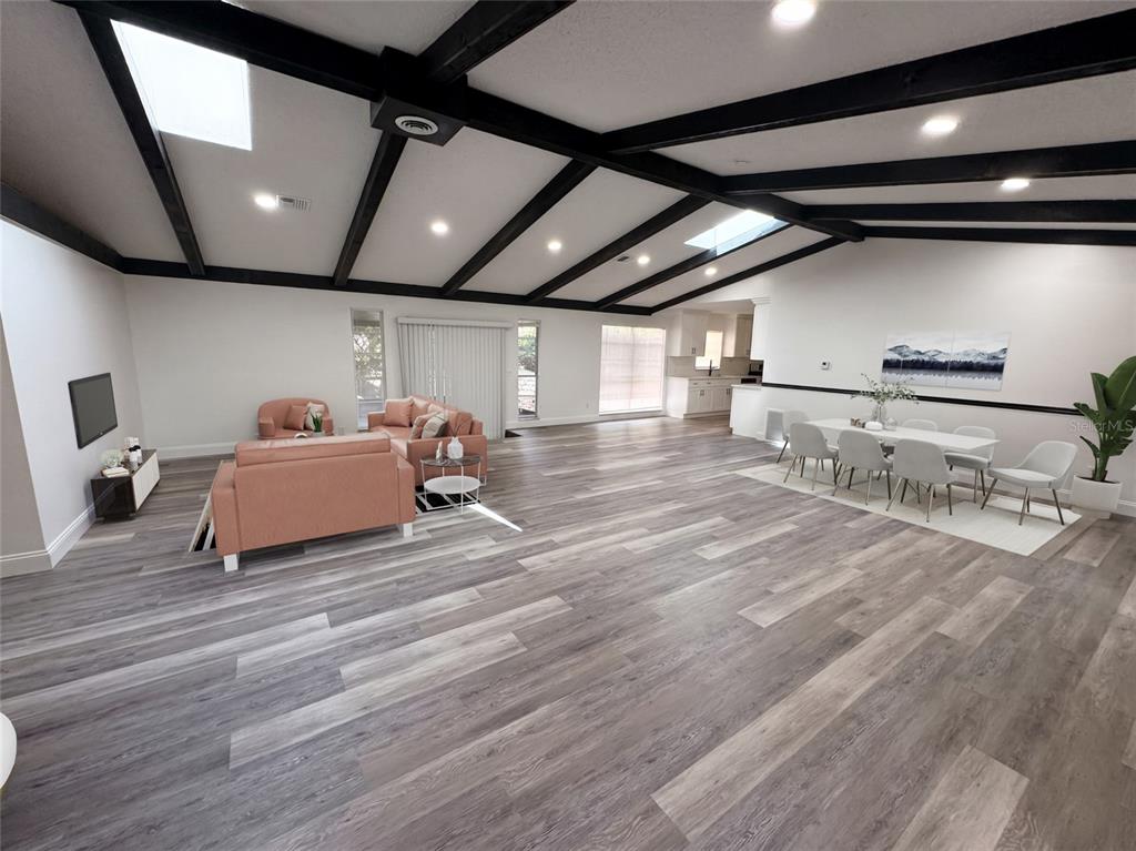 An open-concept living and dining area features vaulted ceilings with exposed black beams and wood-look flooring — 3810 SE 22ND PLACE, OCALA, FL