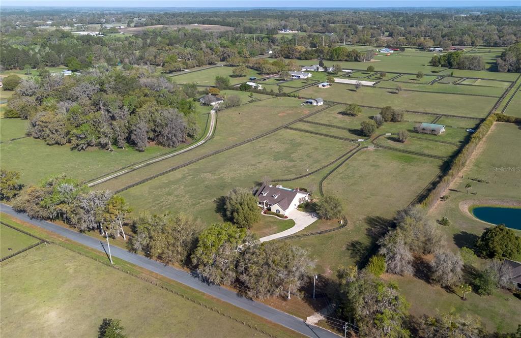 An aerial view shows a house with a pool surrounded by fenced pastures and trees — 8785 NW 63RD STREET, OCALA, FL