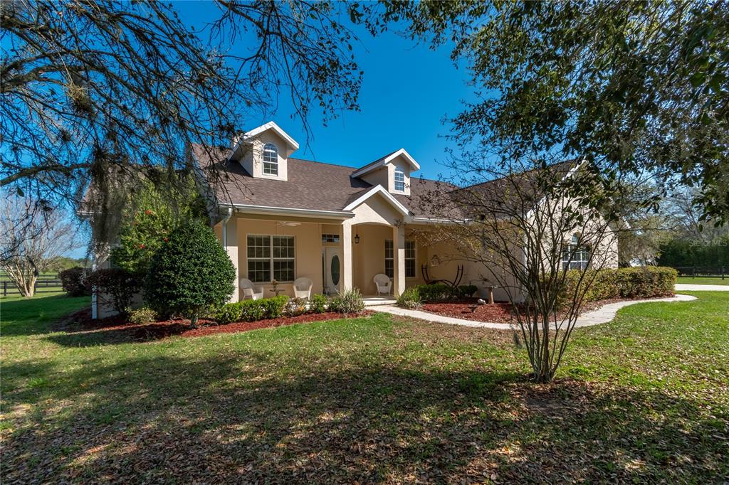 A tan house with a covered porch and two dormer windows sits on a grassy lawn — 8785 NW 63RD STREET, OCALA, FL