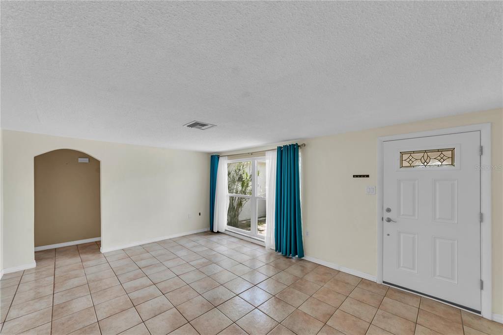 An empty room with light-colored walls, tiled floors, a front door, and a large window — 3401 SUPREME DRIVE, HOLIDAY, FL