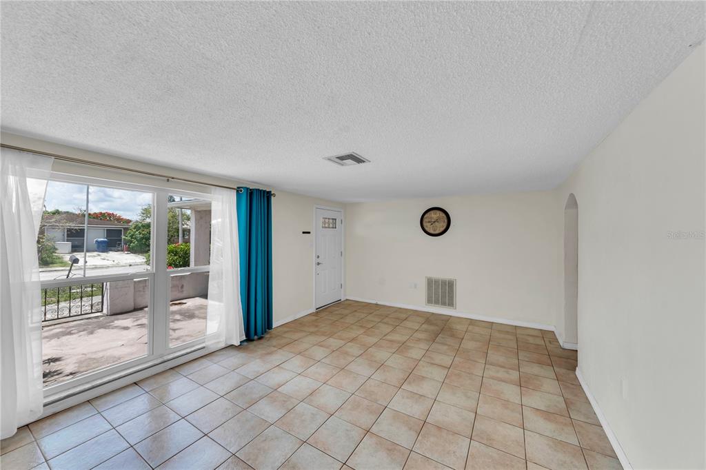 An empty room features beige tile flooring, white walls, a large window, and a door — 3401 SUPREME DRIVE, HOLIDAY, FL