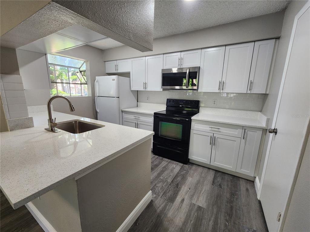 A kitchen features white cabinets, quartz countertops, a black stove, and wood-look flooring — 200 AFTON SQUARE UNIT 108, ALTAMONTE SPRINGS, FL