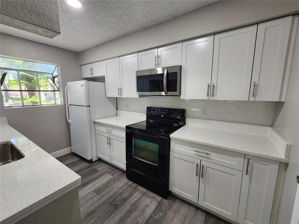 A kitchen features white cabinets, quartz countertops, a black stove, and a white refrigerator — 200 AFTON SQUARE UNIT 108, ALTAMONTE SPRINGS, FL