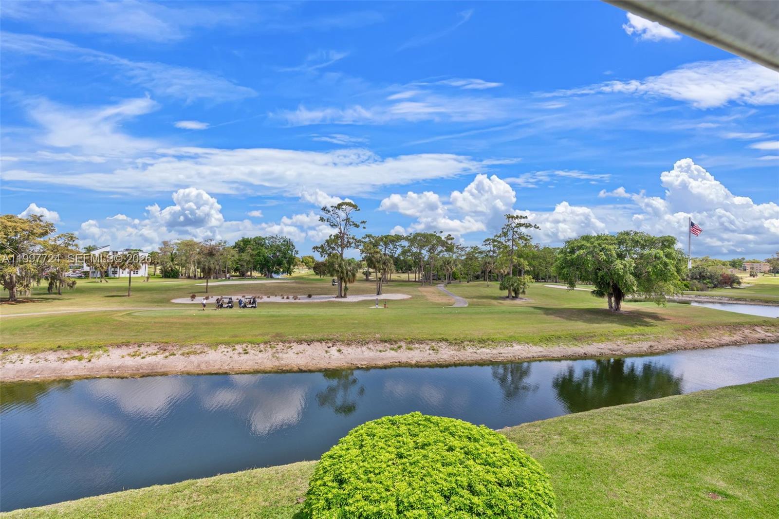 A view of a golf course with a pond, palm trees, and a blue sky — 1480 NW 80th Ave # 304, Margate FL 33063, MARGATE, FL