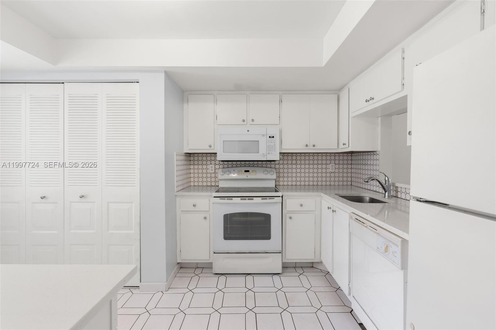 A white kitchen features a stove, microwave, dishwasher, and patterned tile flooring — 1480 NW 80th Ave # 304, Margate FL 33063, MARGATE, FL