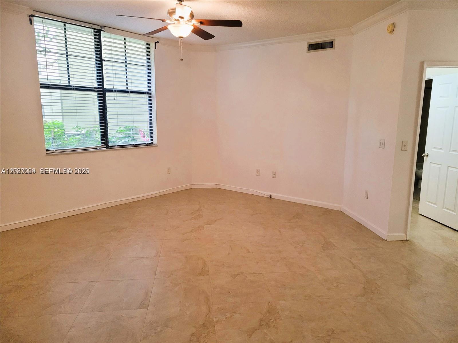 An empty room features beige tile flooring, a ceiling fan, and a large window — 1919 Van Buren St # 111A, Hollywood FL 33020, HOLLYWOOD, FL