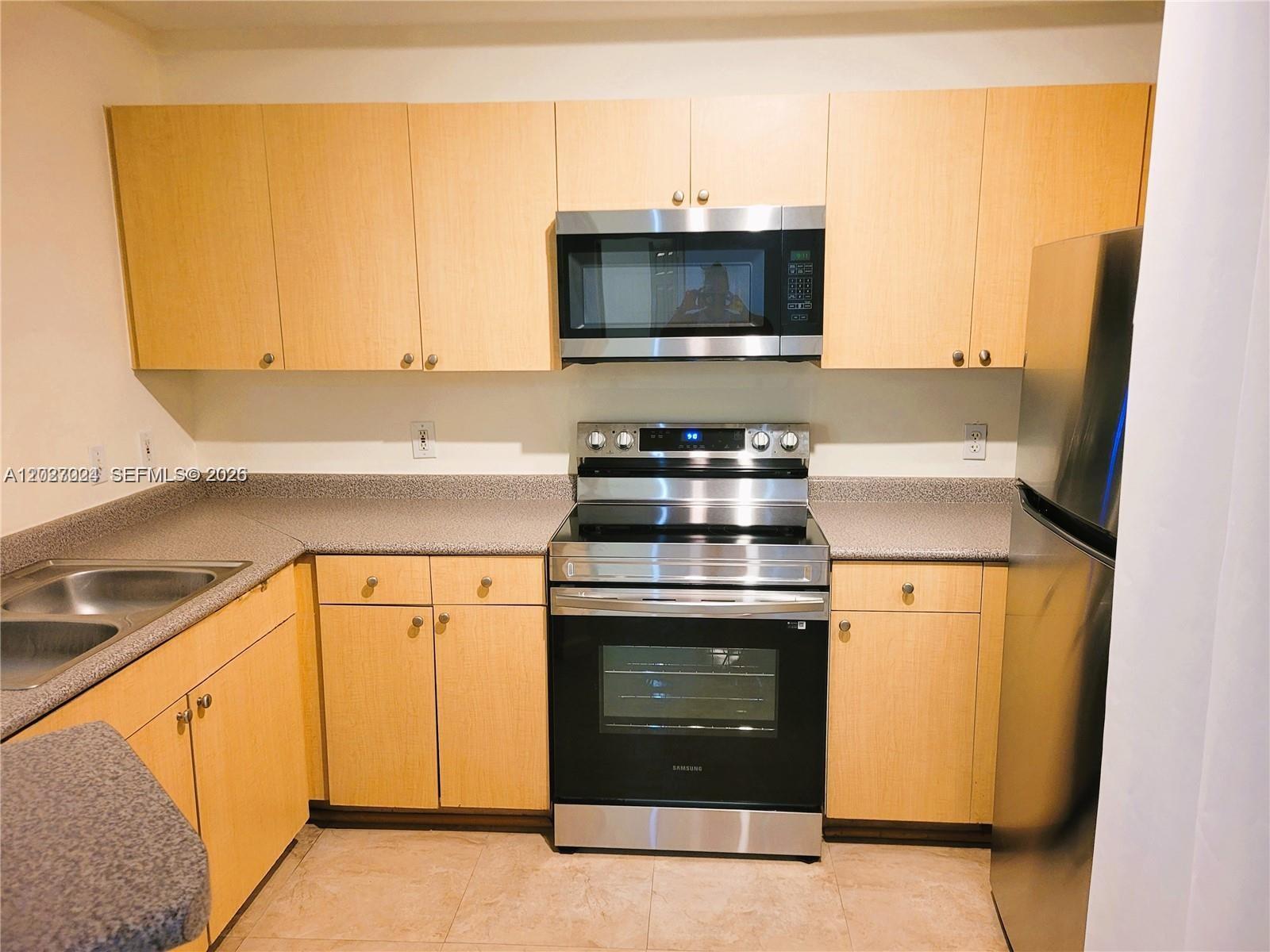 A kitchen features light wood cabinets, stainless steel appliances, and gray speckled countertops — 1919 Van Buren St # 111A, Hollywood FL 33020, HOLLYWOOD, FL