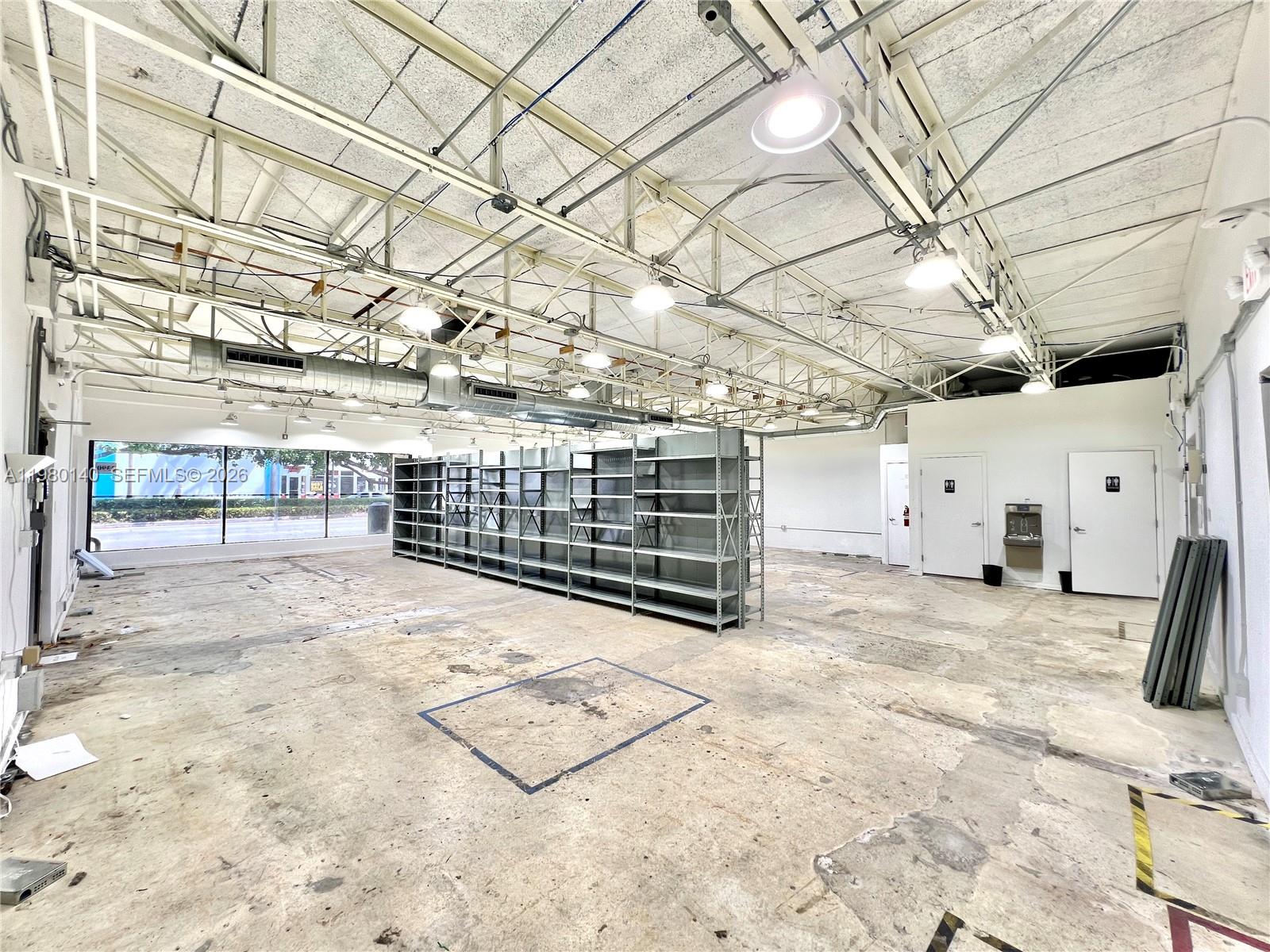 An empty commercial space features exposed ceiling trusses, concrete floors, and metal shelving units — 3390 SW Coral Way, Miami FL 33142, MIAMI, FL