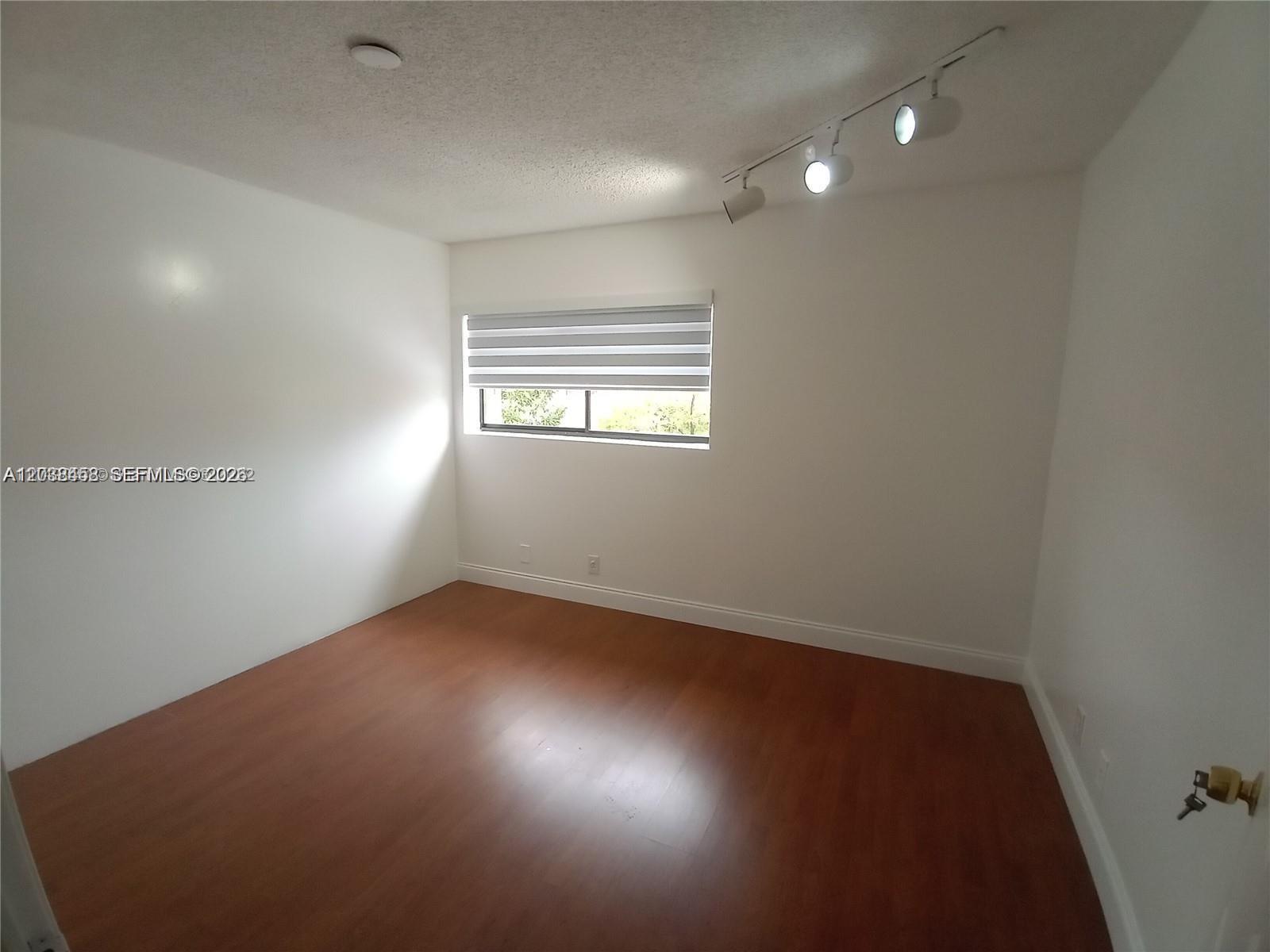 An empty room features white walls, wood-look flooring, a window with blinds, and track lighting — 6533 NW 170th Ln, Hialeah FL 33015, HIALEAH, FL