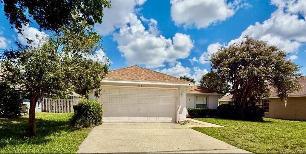 A single-story house with a two-car garage and a concrete driveway under a blue sky — 142 GLASGOW COURT, DAVENPORT, FL