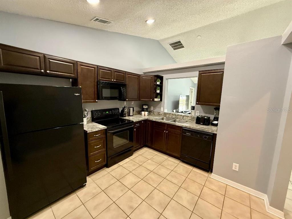 A kitchen features dark wood cabinets, black appliances, granite countertops, and light-colored tile flooring — 142 GLASGOW COURT, DAVENPORT, FL