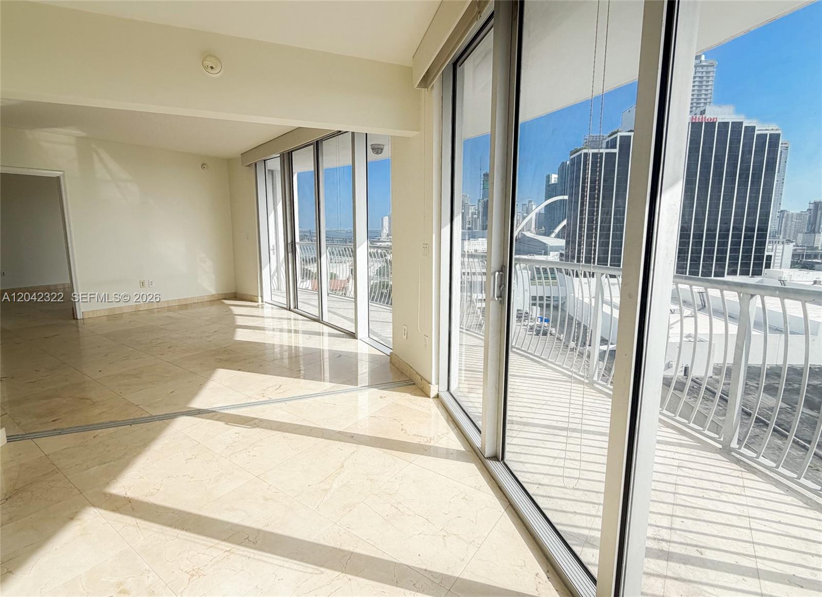 An empty room with light-colored tile flooring features large sliding glass doors opening to a balcony — 1750 N Bayshore Dr # 1814, Miami FL 33132, MIAMI, FL