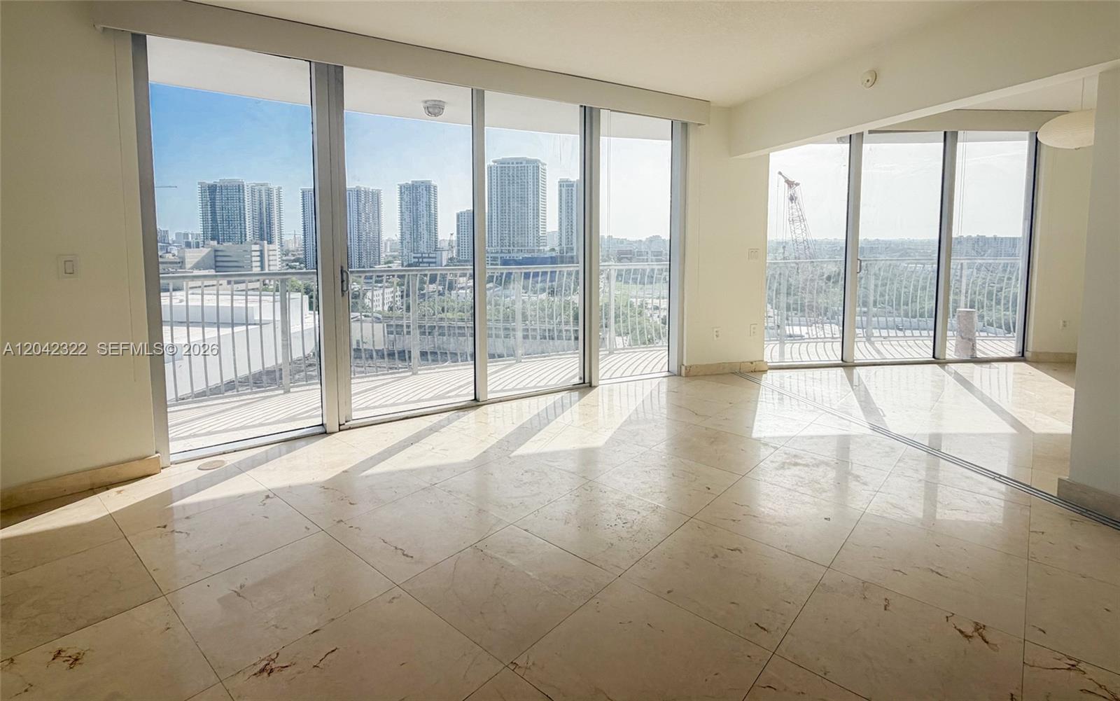 An empty room features light-colored tile floors and floor-to-ceiling windows overlooking a city skyline — 1750 N Bayshore Dr # 1814, Miami FL 33132, MIAMI, FL