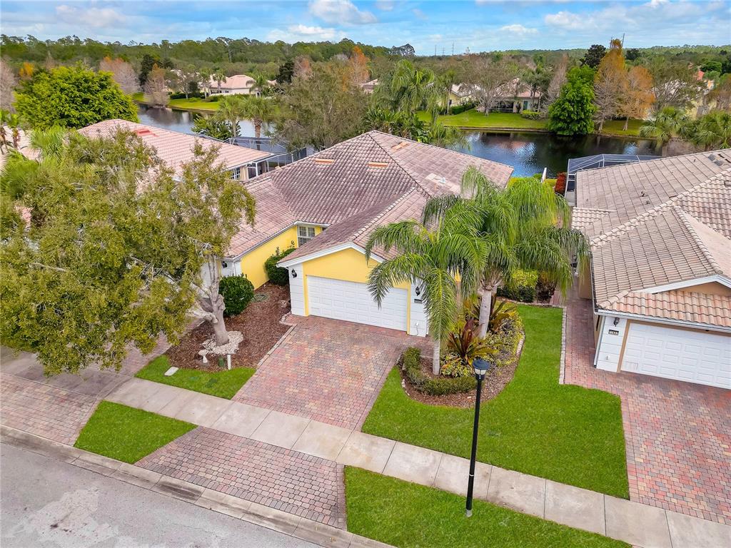 An aerial view shows a yellow house with a tiled roof, garage, and paver driveway — 11831 FAN TAIL LANE, ORLANDO, FL