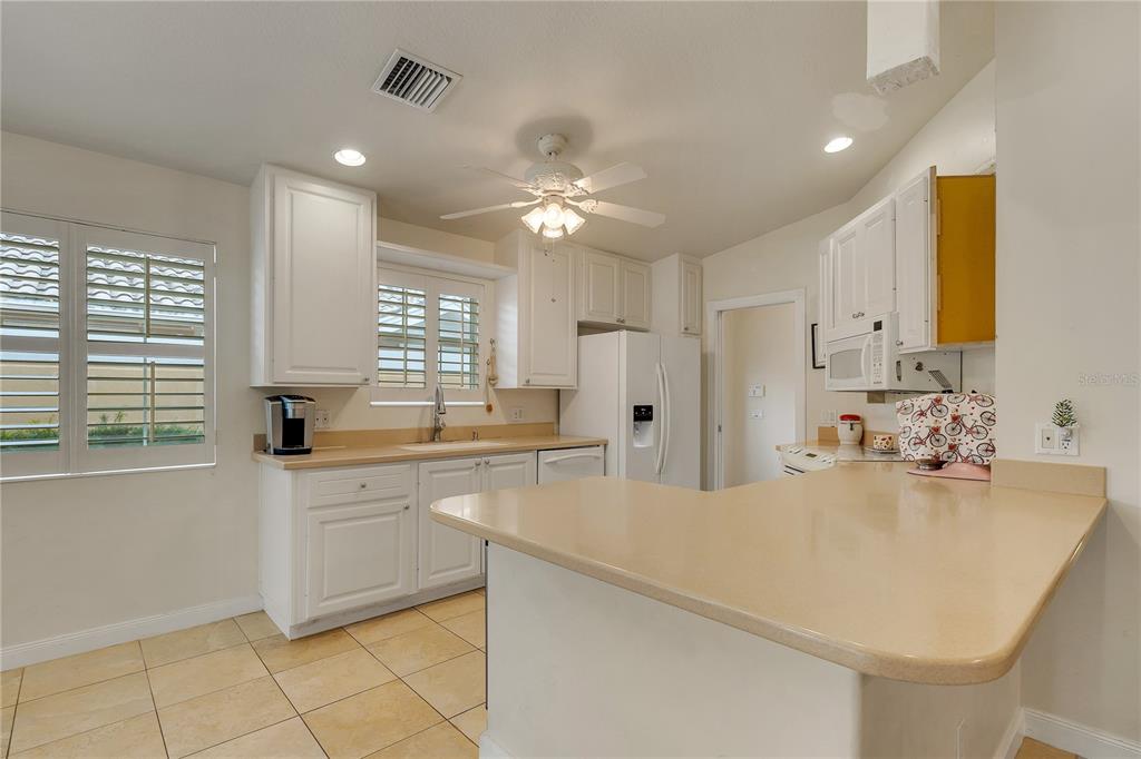 A kitchen features white cabinets, beige countertops, tile flooring, and a ceiling fan — 11831 FAN TAIL LANE, ORLANDO, FL