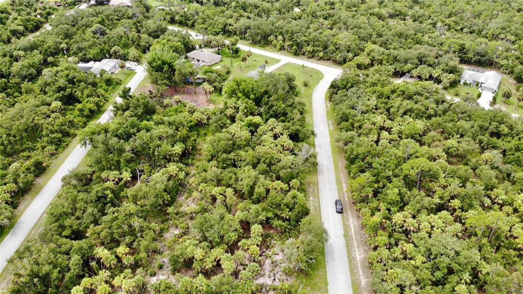 An aerial view shows a paved road winding through a dense, wooded residential area — 3144 MATHEW STREET, PORT CHARLOTTE, FL
