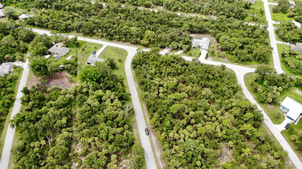 An aerial view shows a residential neighborhood with houses surrounded by dense, wooded vegetation — 3144 MATHEW STREET, PORT CHARLOTTE, FL