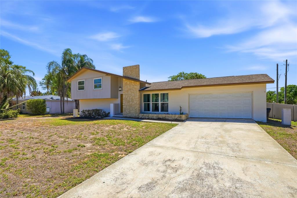 A split-level house with a stone chimney, beige siding, and a concrete driveway — 721 VILLAGE PLACE, BRANDON, FL