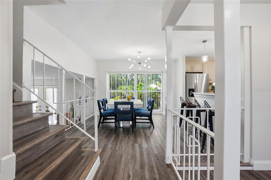 A dining area with blue chairs and a modern chandelier sits beside a wooden staircase — 721 VILLAGE PLACE, BRANDON, FL