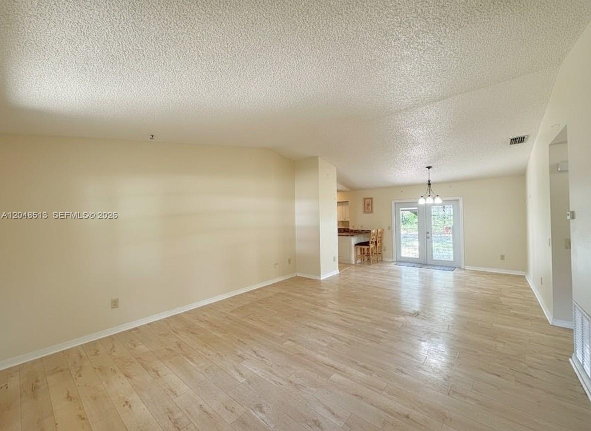 An empty living room features light wood-look flooring, beige walls, and a vaulted ceiling — 4005 E Sunflower Cir, La Belle FL 33935, LA BELLE, FL