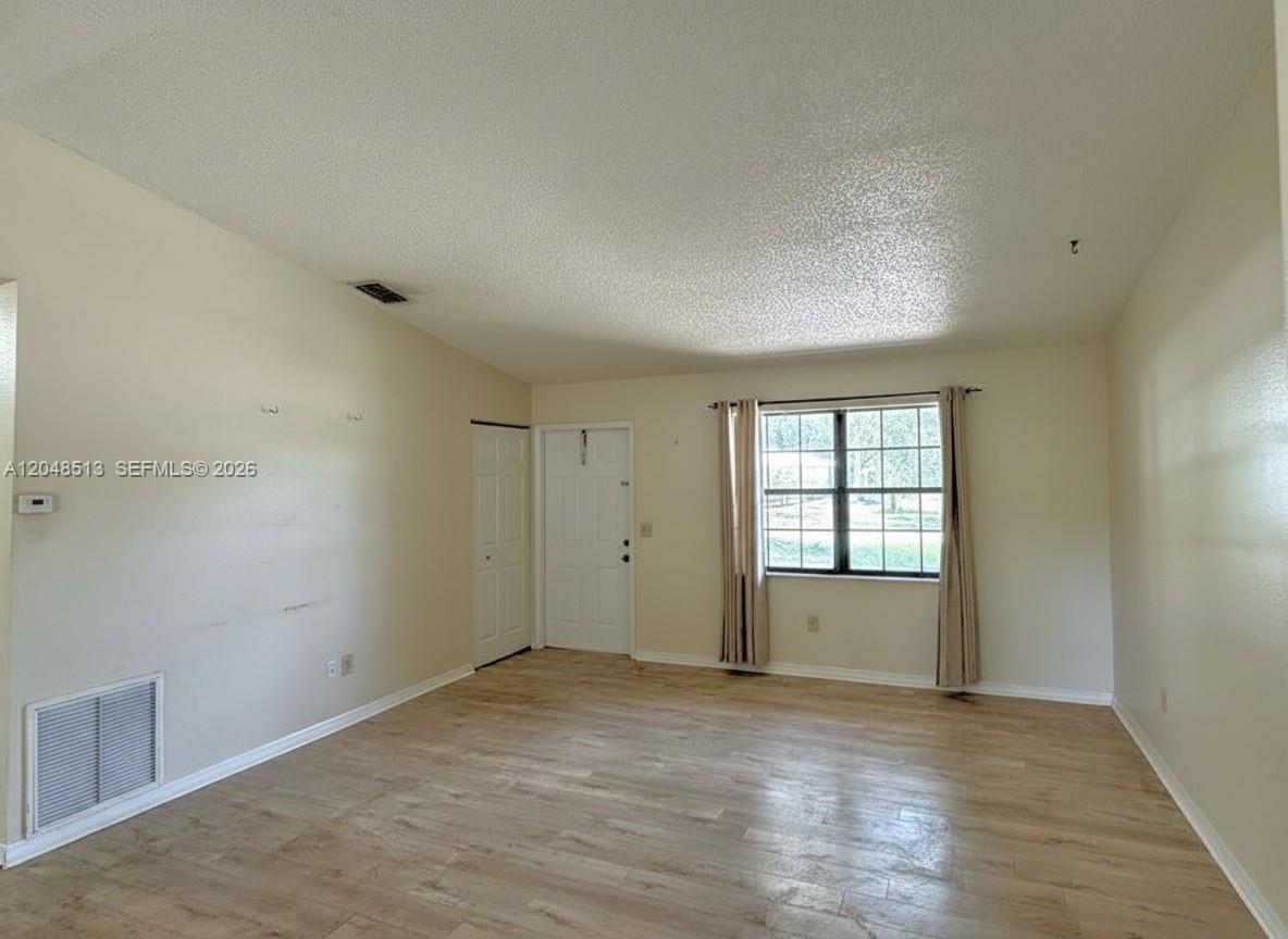 An empty living room features light wood-look flooring, beige walls, and a single window — 4005 E Sunflower Cir, La Belle FL 33935, LA BELLE, FL