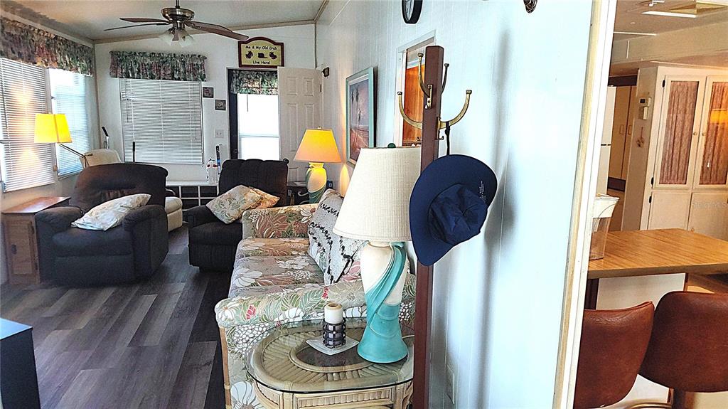 A living room with a floral sofa, two recliners, and a coat rack near a kitchen — 3300 26TH AVENUE E UNIT 201, BRADENTON, FL