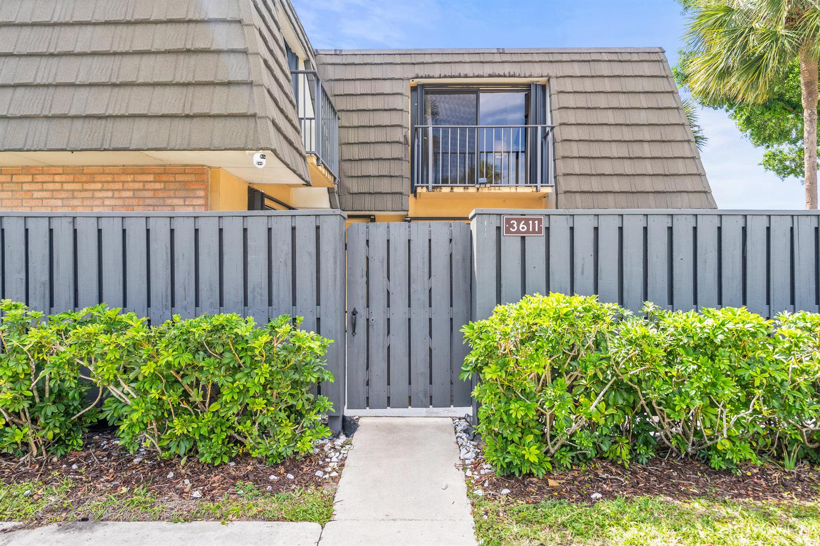 A gray wooden fence and gate lead to a two-story building with a balcony — 3611 36th Way, West Palm Beach FL 33407, WEST PALM BEACH, FL