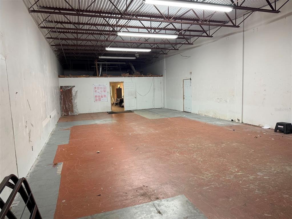 An empty industrial warehouse space features a red concrete floor and exposed metal ceiling trusses — 10949 SW 93RD TERRACE UNIT 203, OCALA, FL