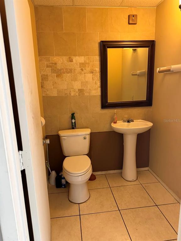 A small bathroom features a pedestal sink, a white toilet, and tan tiled walls — 10949 SW 93RD TERRACE UNIT 203, OCALA, FL