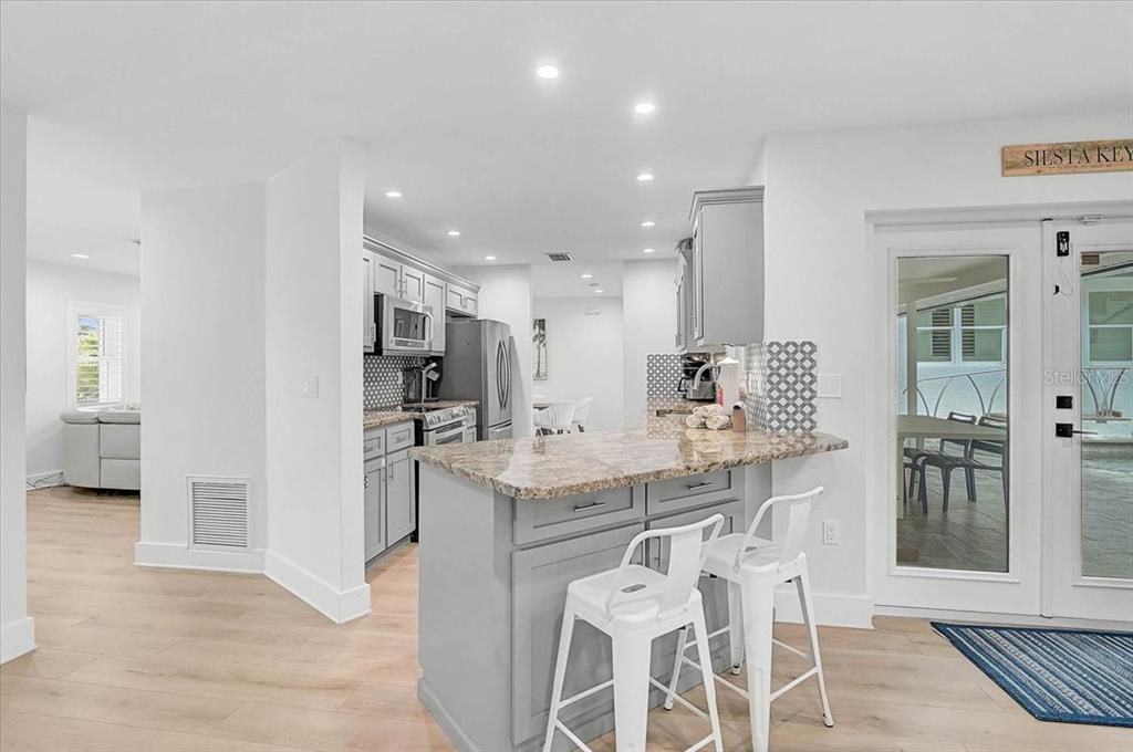 A kitchen features gray cabinets, granite countertops, stainless steel appliances, and a patterned tile backsplash — 3515 LA PALOMA AVENUE, SARASOTA, FL