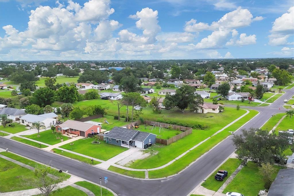 An aerial view shows a suburban neighborhood with single-family homes, green lawns, and paved streets — 7590 LYNCREST STREET, NORTH PORT, FL