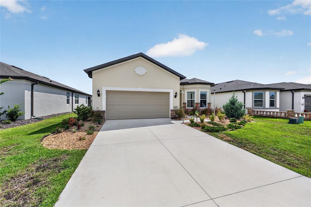 A single-story suburban house with a tan garage, beige stucco siding, and a concrete driveway — 8644 SW 59TH LANE ROAD, OCALA, FL