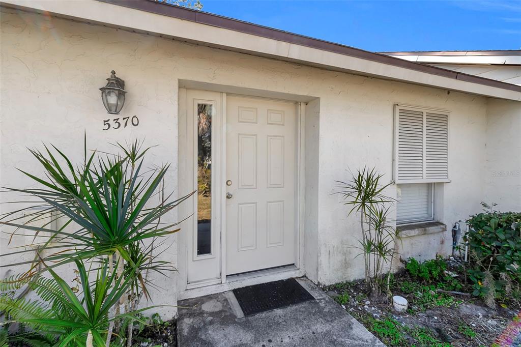 The exterior of a house features a white front door, a side window, and landscaping — 5370 ROYAL PALM AVENUE UNIT 5370, SARASOTA, FL